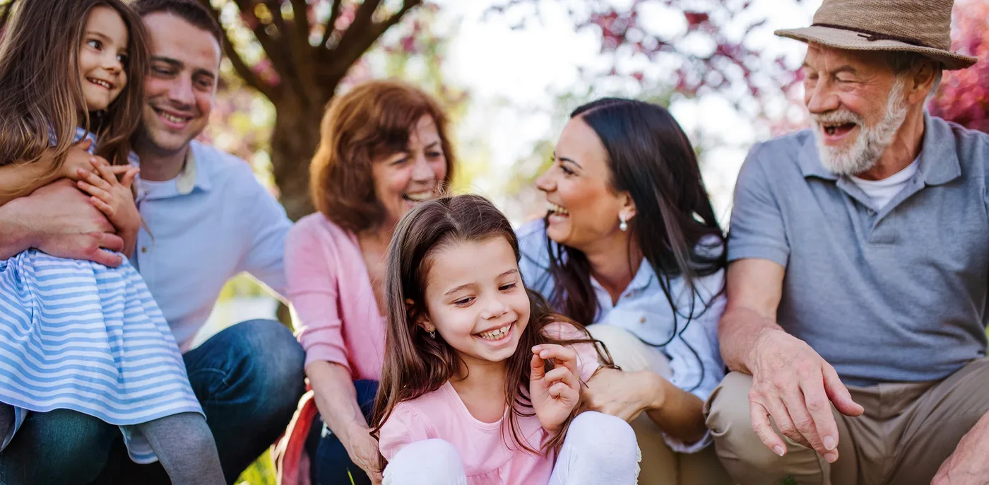 Three generations of a family laughing together outdoors under a flowering dogwood tree